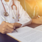 Physician doctor writing on medical health care record, patients discharge, or prescription form paperwork in hospital clinic discussing success medical healthcare, Medicine doctor's working concept