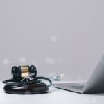 Gavel and stethoscope placed near a laptop, symbolizing legal and healthcare intersection