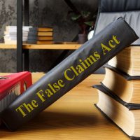 A book titled "The False Claims Act" leaning on a stack of books with a binder nearby.